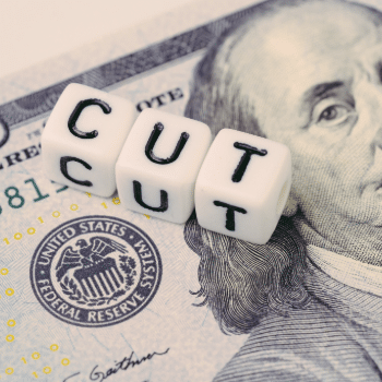 letter cubes spelling "CUT" placed on U.S. currency, symbolizing a Federal Reserve interest rate cut and its effect on technology and embedded systems markets