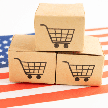 stacked boxes with shopping cart icons on american flag representing buy america compliance and domestic manufacturing
